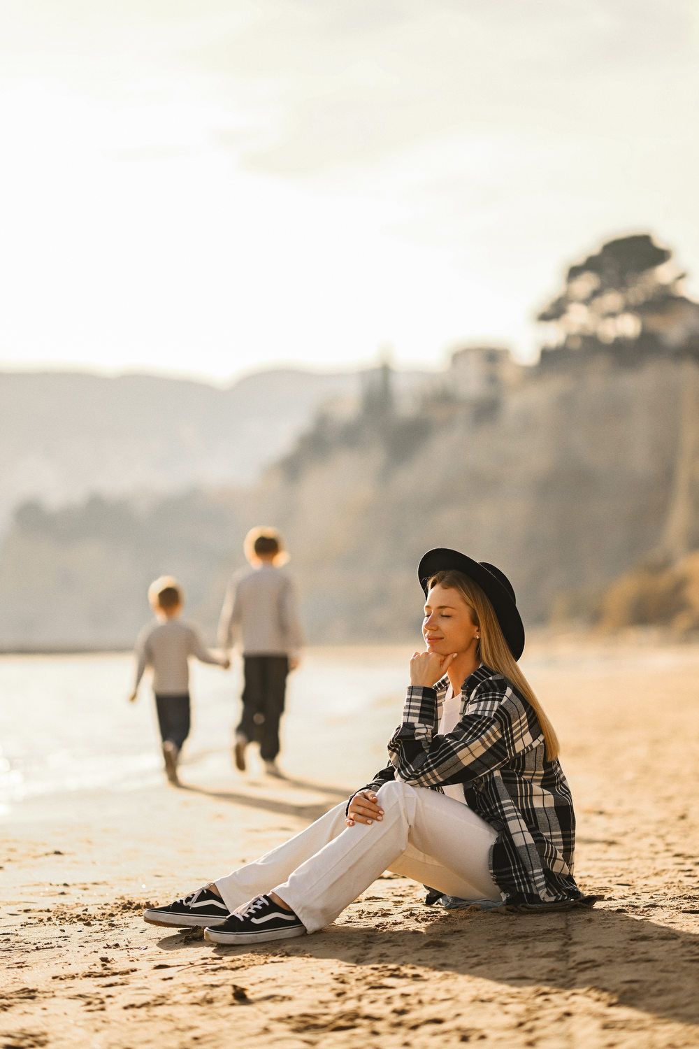A mother relaxing on the sand with her eyes closed in the golden sun while her children play in the background in Calpe