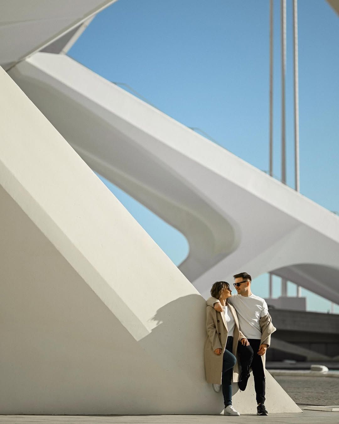 Editorial love story session with a couple leaning against the massive white modern architecture in Valencia under blue skies.