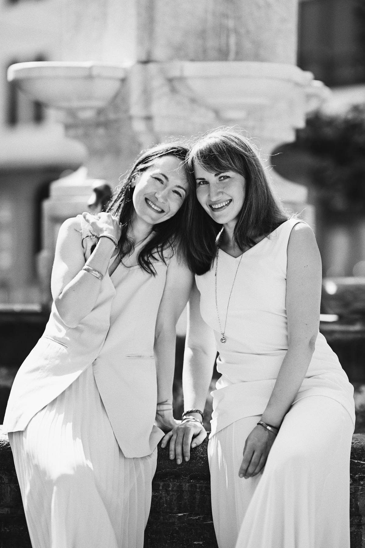 Black and white close-up portrait of two smiling sisters leaning against a stone fountain structure.