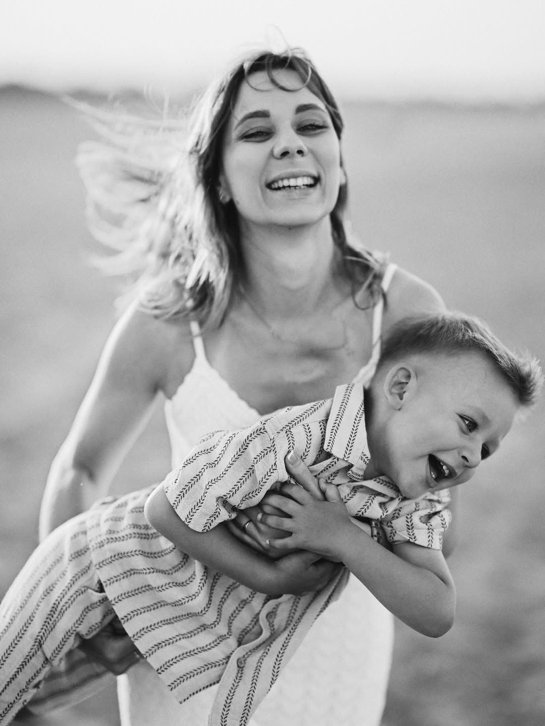 Black and white portrait of a mother holding her laughing toddler during a candid family moment on the beach in Valencia.
