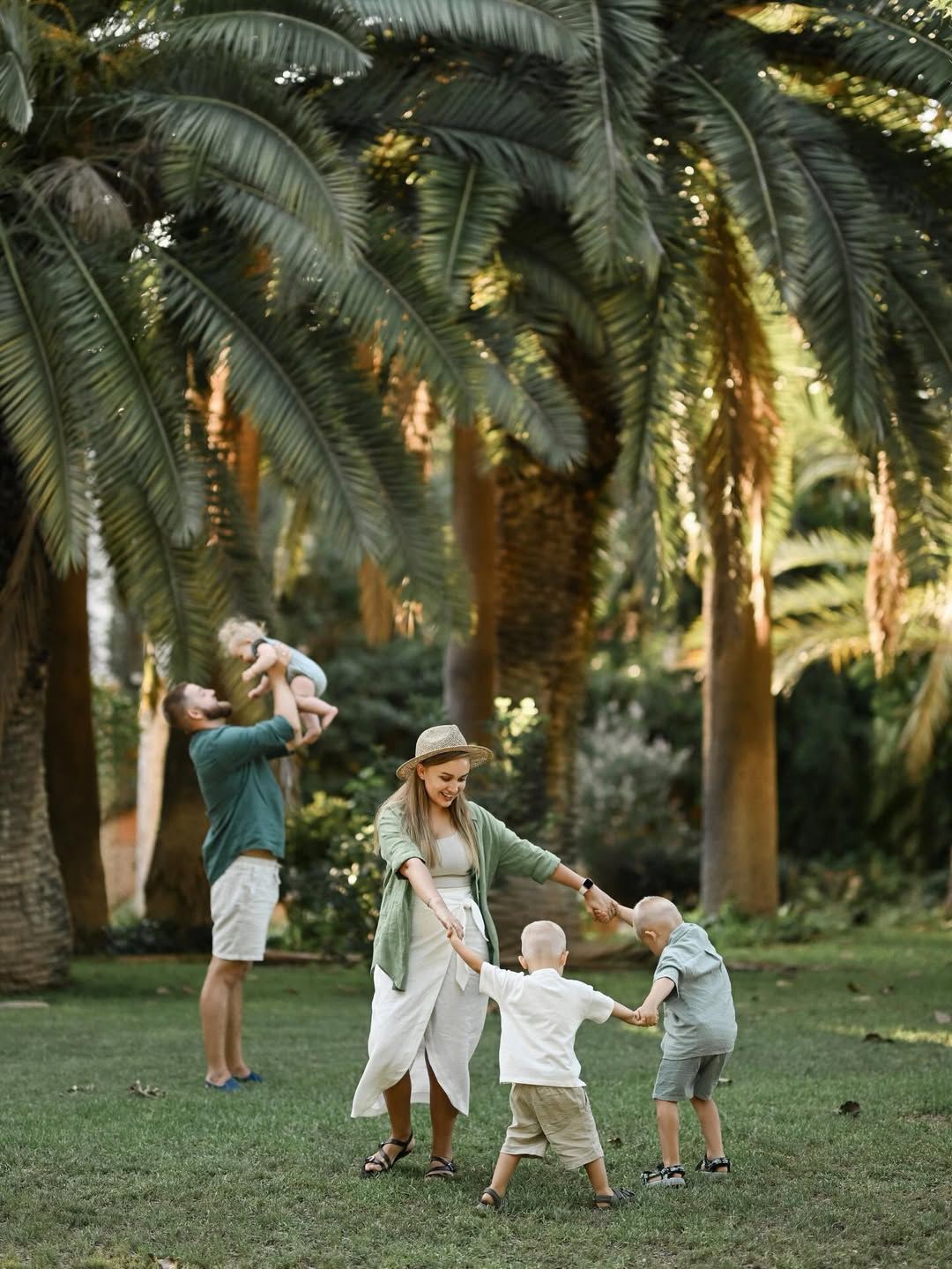 Parents and children holding hands and playing under large palm trees during a family photoshoot in Turia Park.