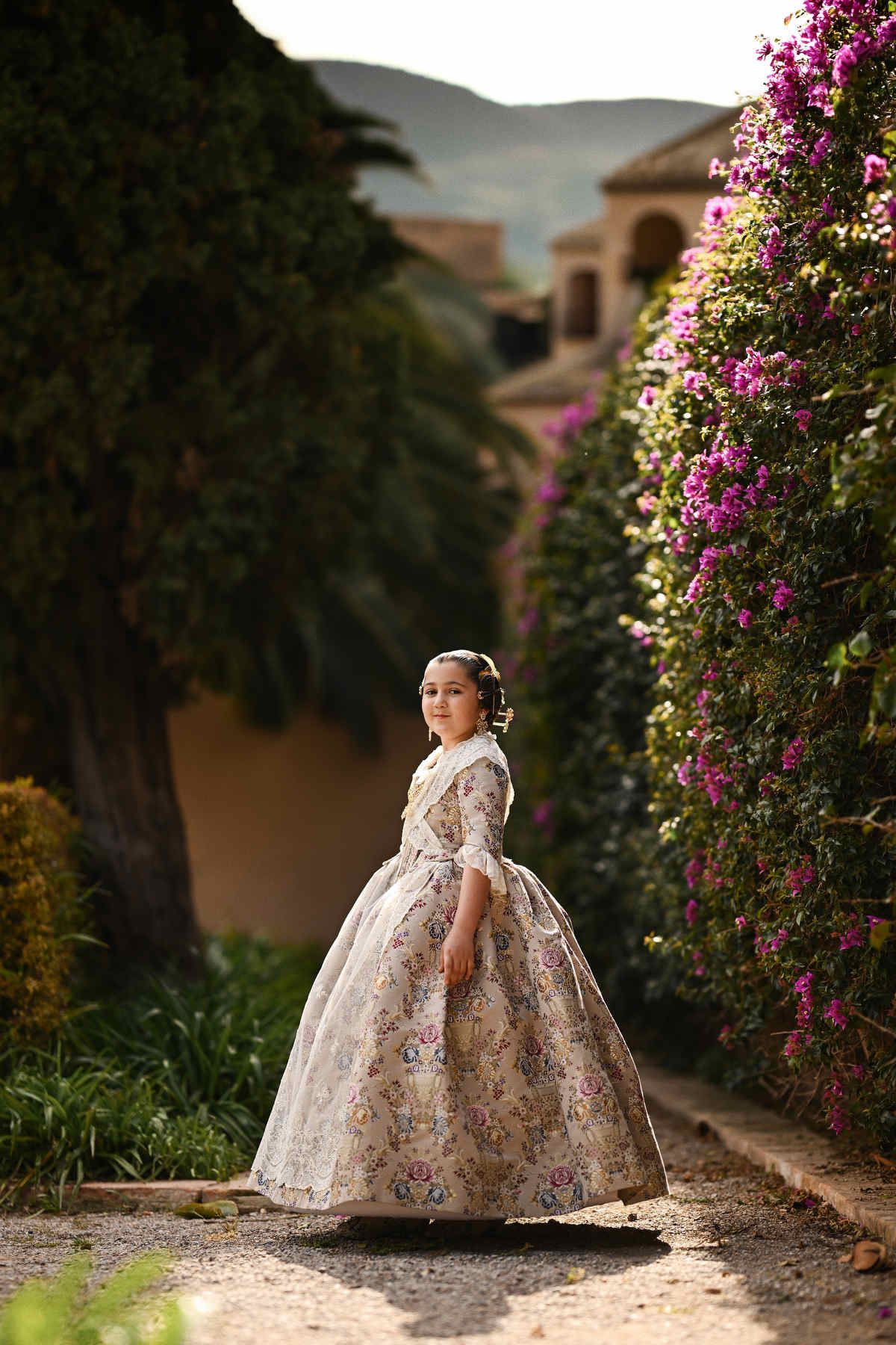 A full-body portrait of a young girl in an authentic Valencian Fallera outfit, standing elegantly amidst the neoclassical gardens
