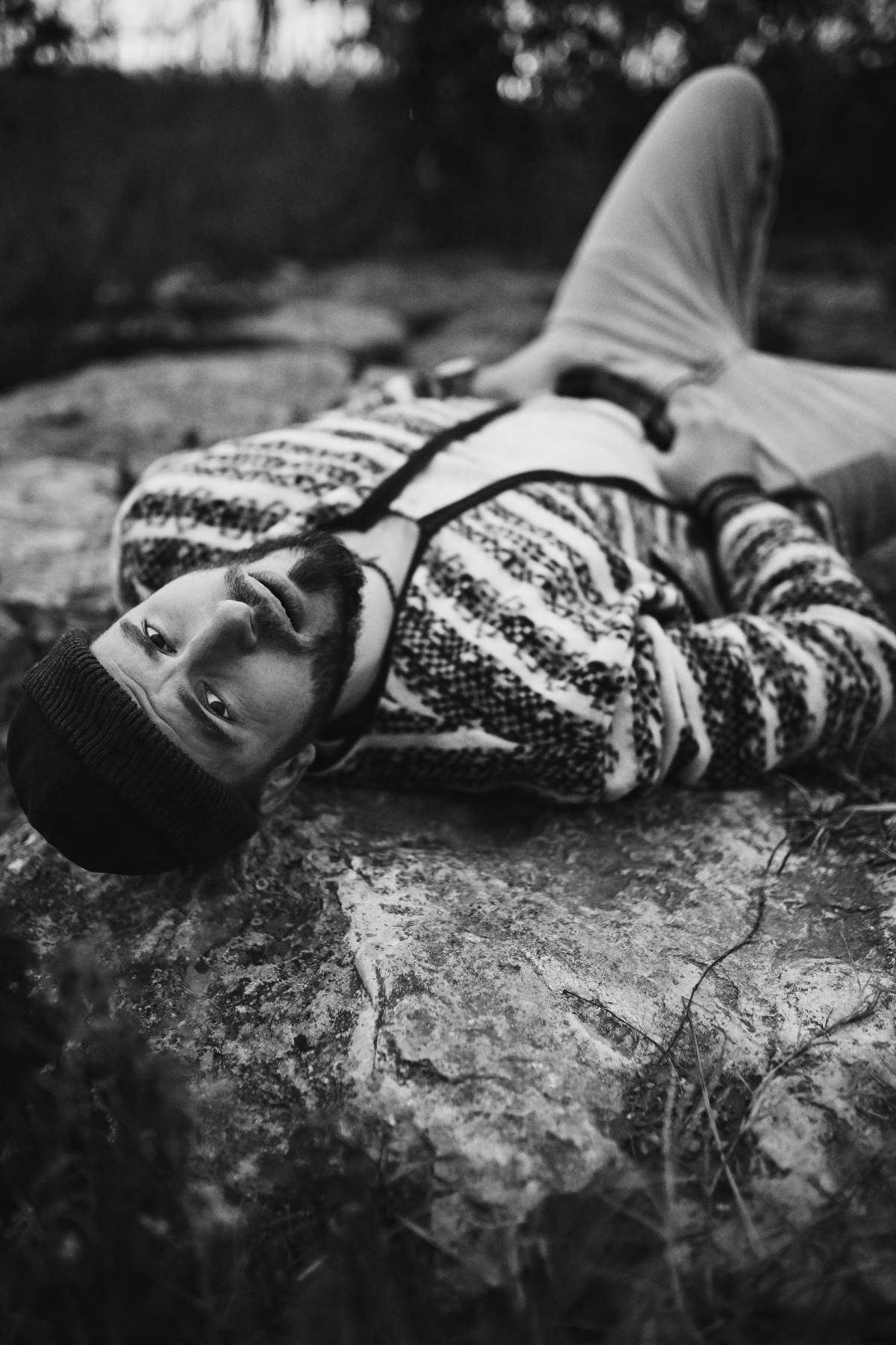 Relaxed yet brutal male portrait of a man lying on a rock, looking directly at the camera during an outdoor photoshoot.