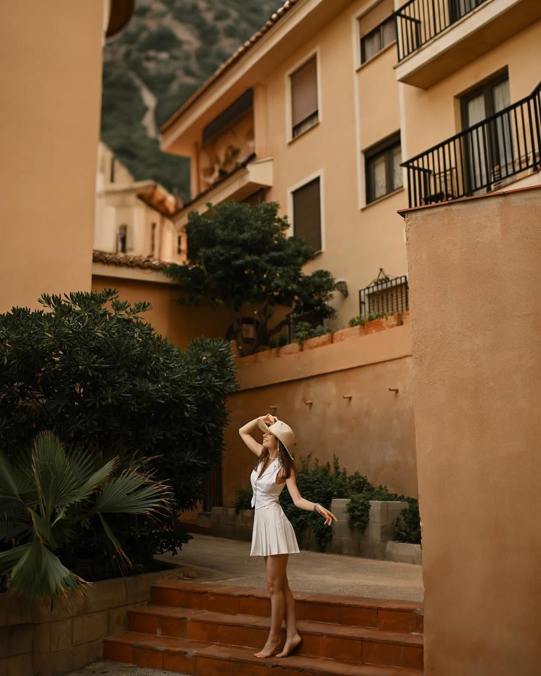 A woman in a short skirt poses dynamically against the vibrant, colorful facades and unique coastal architecture of Port Saplaya