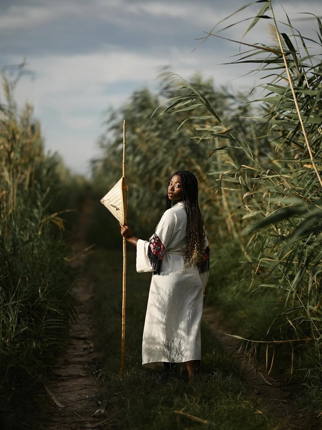 A woman turns to look back at the photographer while standing in a dense green pathway of tall reeds in Albufera park