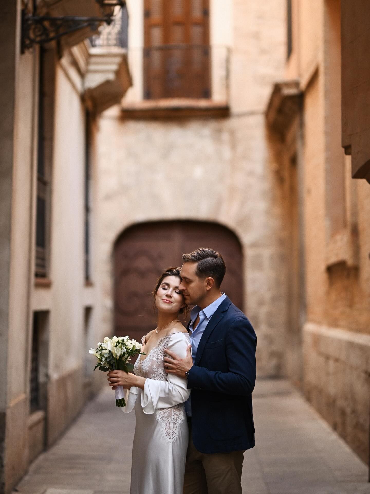 An intimate moment of a groom embracing his bride from behind in a quiet, sunlit alley of Valencia's historic center.