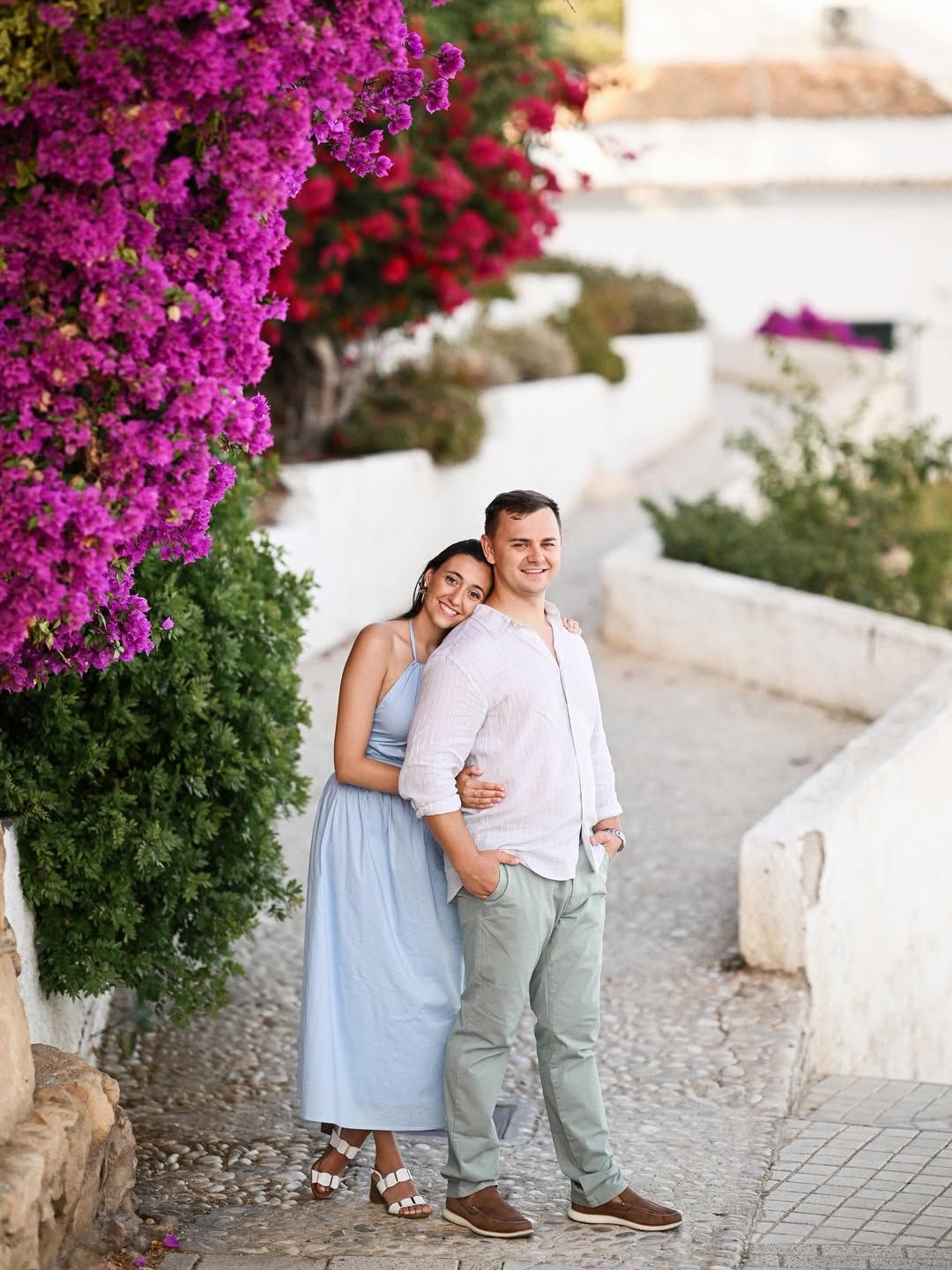 A romantic portrait of an engaged couple standing beside a vibrant blooming bush in the narrow, picturesque streets of Valencia city.