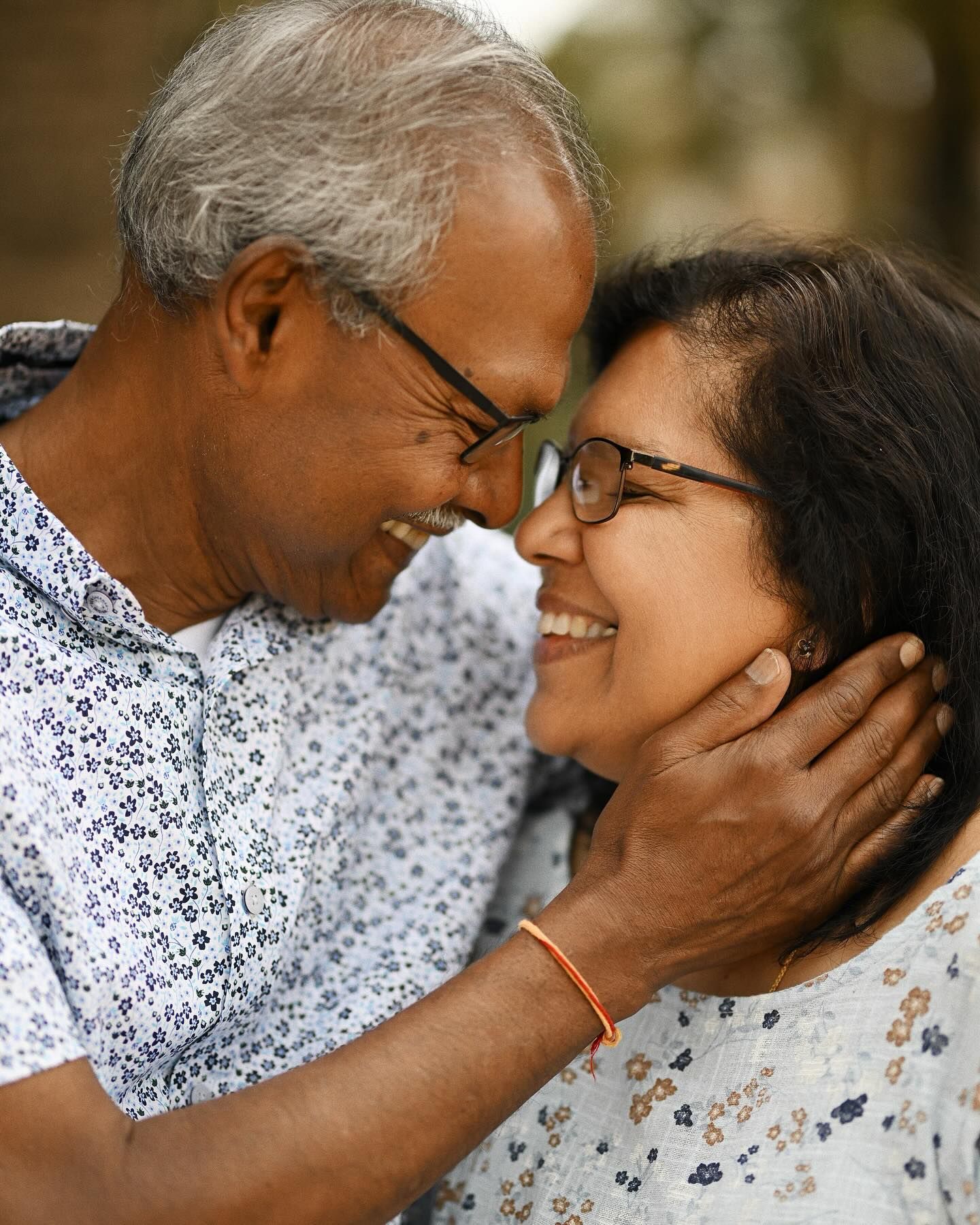 An intimate and affectionate close-up portrait of an elderly couple smiling at each other, with the husband gently touching his wife's face.