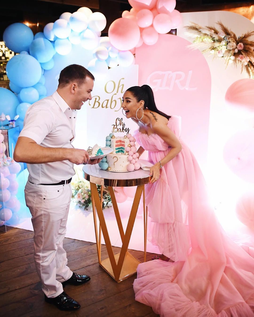 Happy expecting couple cutting their two-tier gender reveal cake to discover a blue sponge inside, announcing a baby boy.