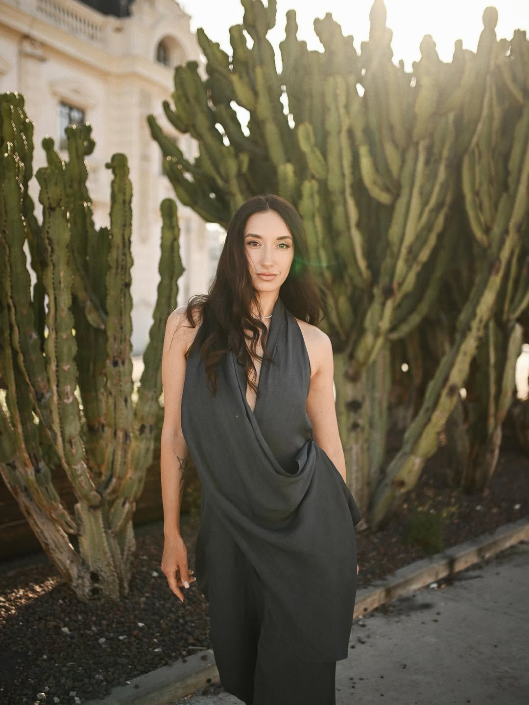 Fashion portrait of a brunette woman in a dark dress standing in front of tall green cacti near Valencia Marina