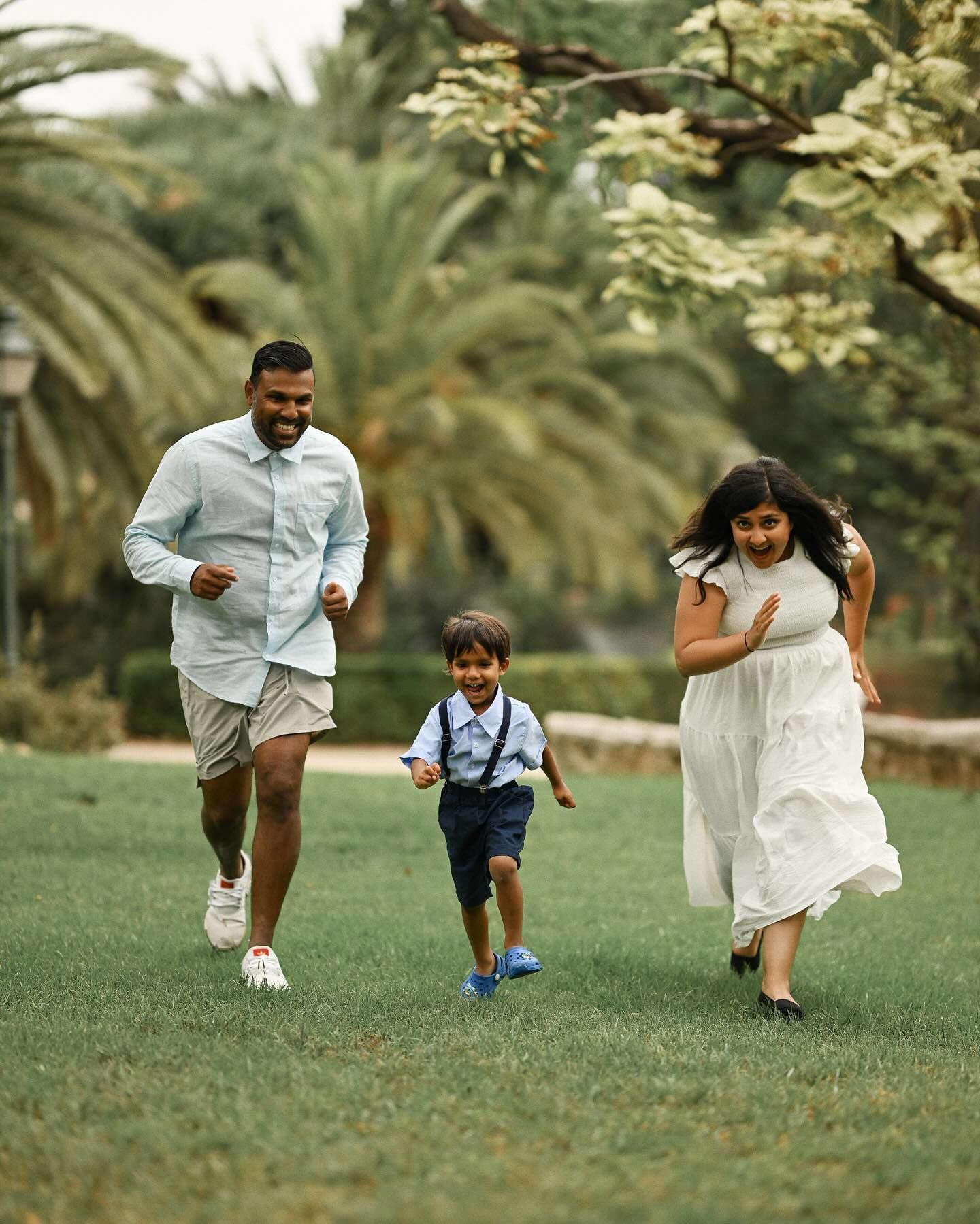 Parents playfully running across the grass with their young son in a park, capturing a moment of genuine happiness and active family fun.