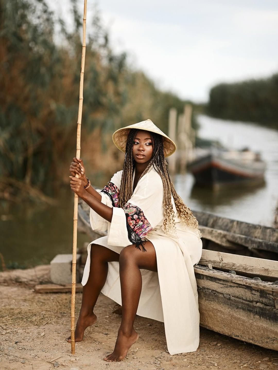 A woman in a stylized white robe posing inside a traditional wooden fishing boat on the calm water of Albufera lake