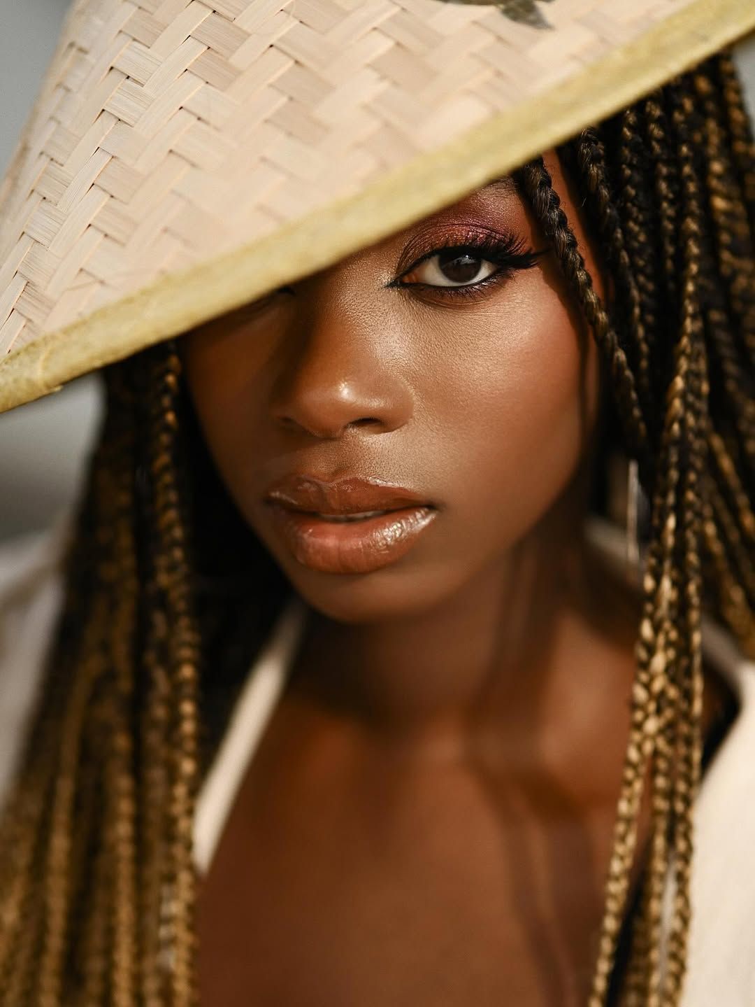 High-fashion editorial portrait of a woman looking out from underneath a traditional straw hat with a bold makeup look