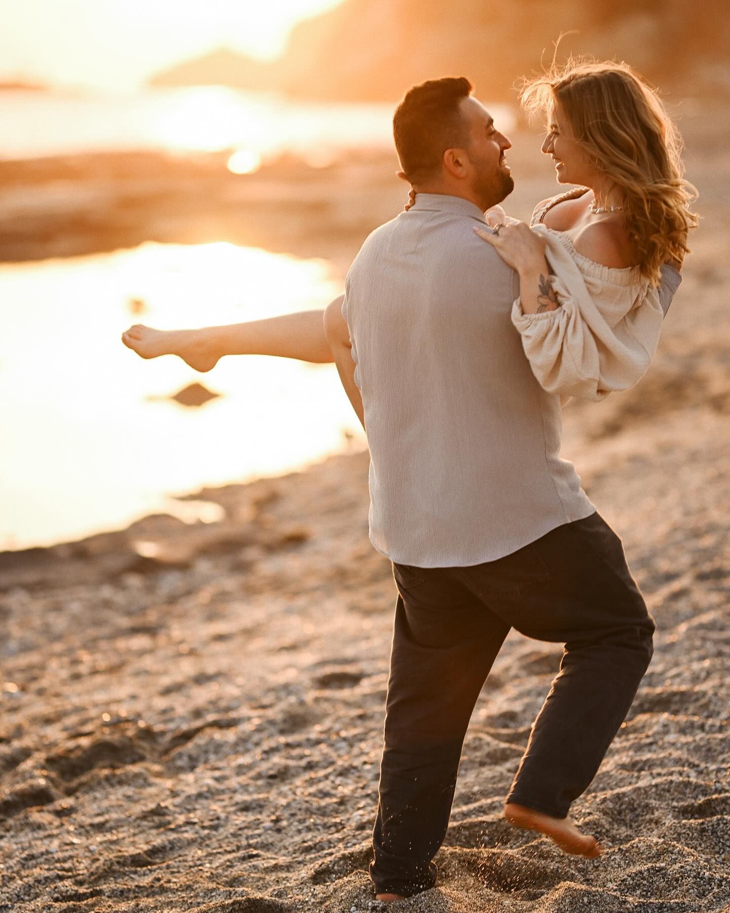 A man carrying his smiling wife in his arms on a sandy beach during golden hour in Costa Blanca.