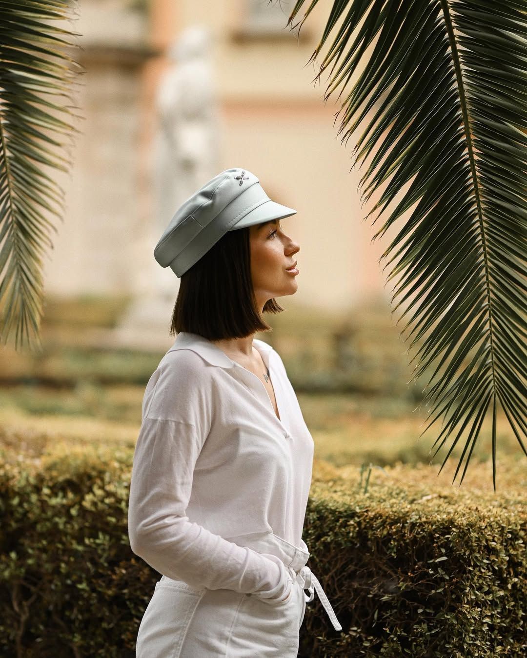 Profile view of a woman wearing a light cap standing near tropical palm leaves in Valencia.