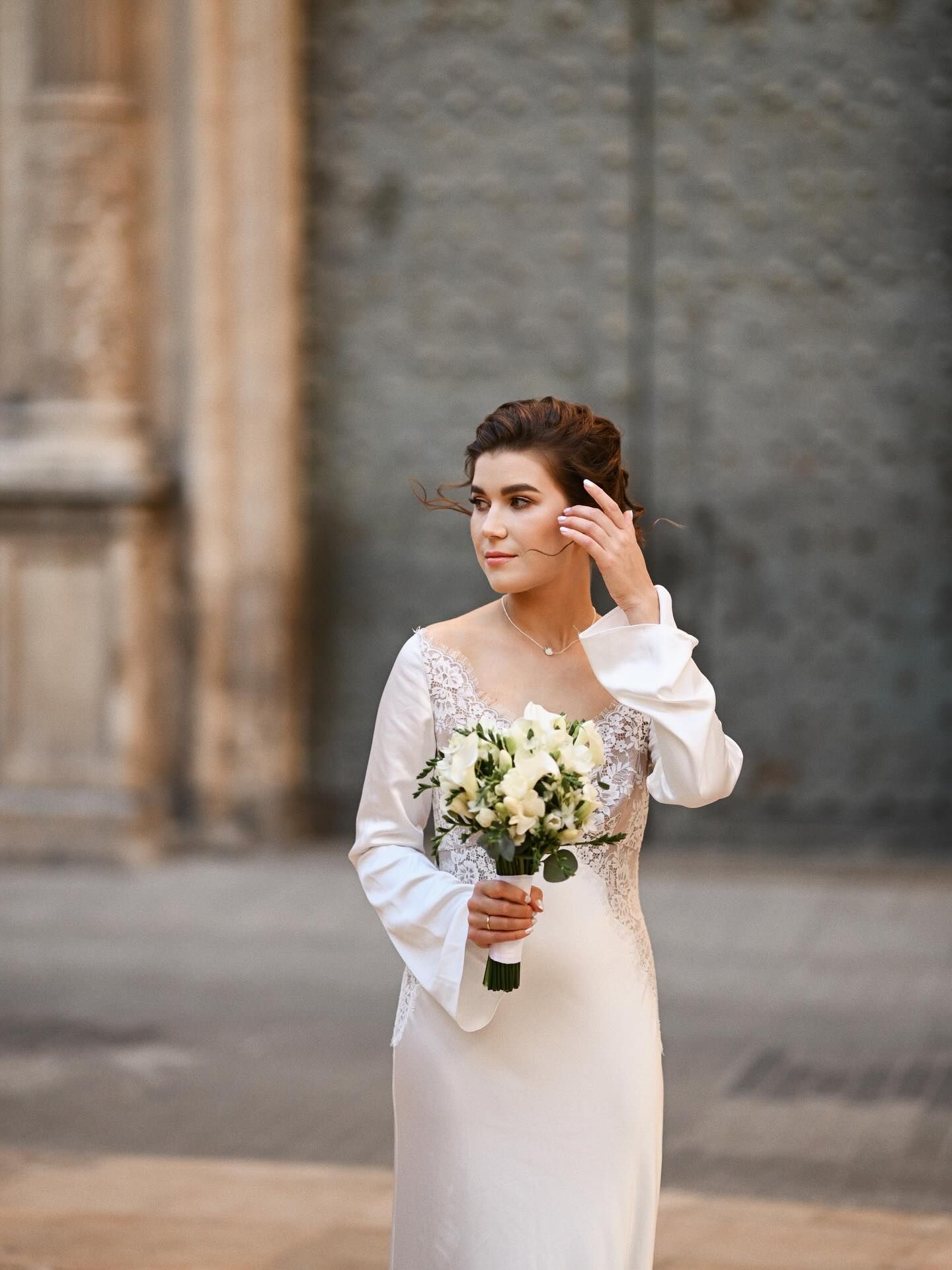 Close-up portrait of a bride in an elegant silk dress with lace details, holding a bouquet against an antique stone wall in Valencia.