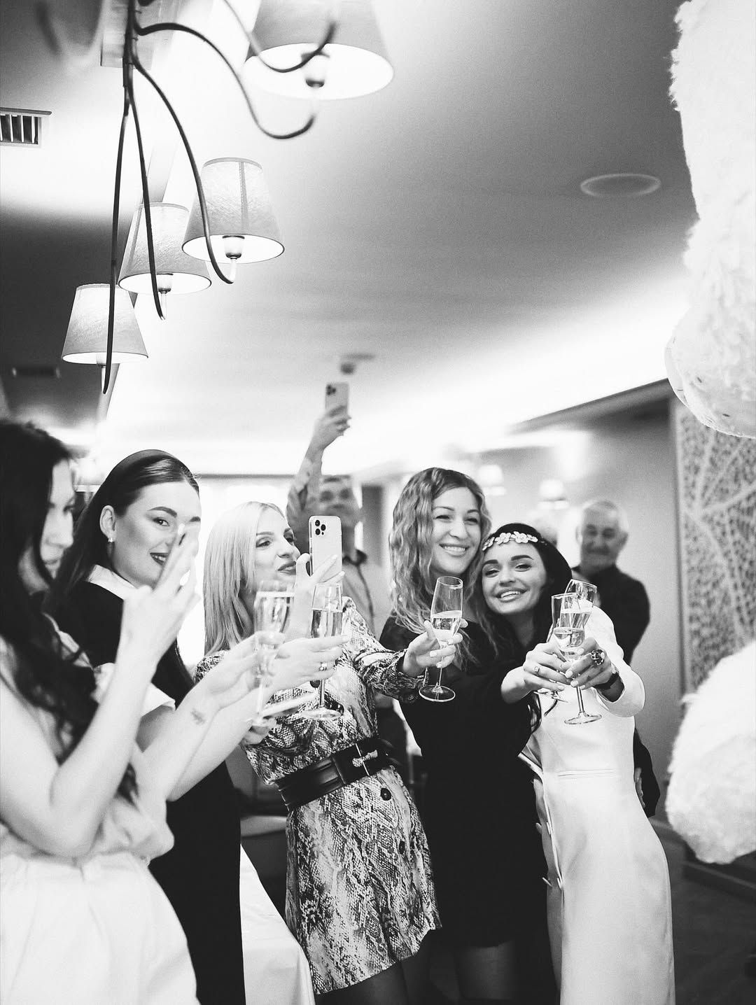 Black and white photography of adult guests sipping champagne at a high-end kids' birthday party.