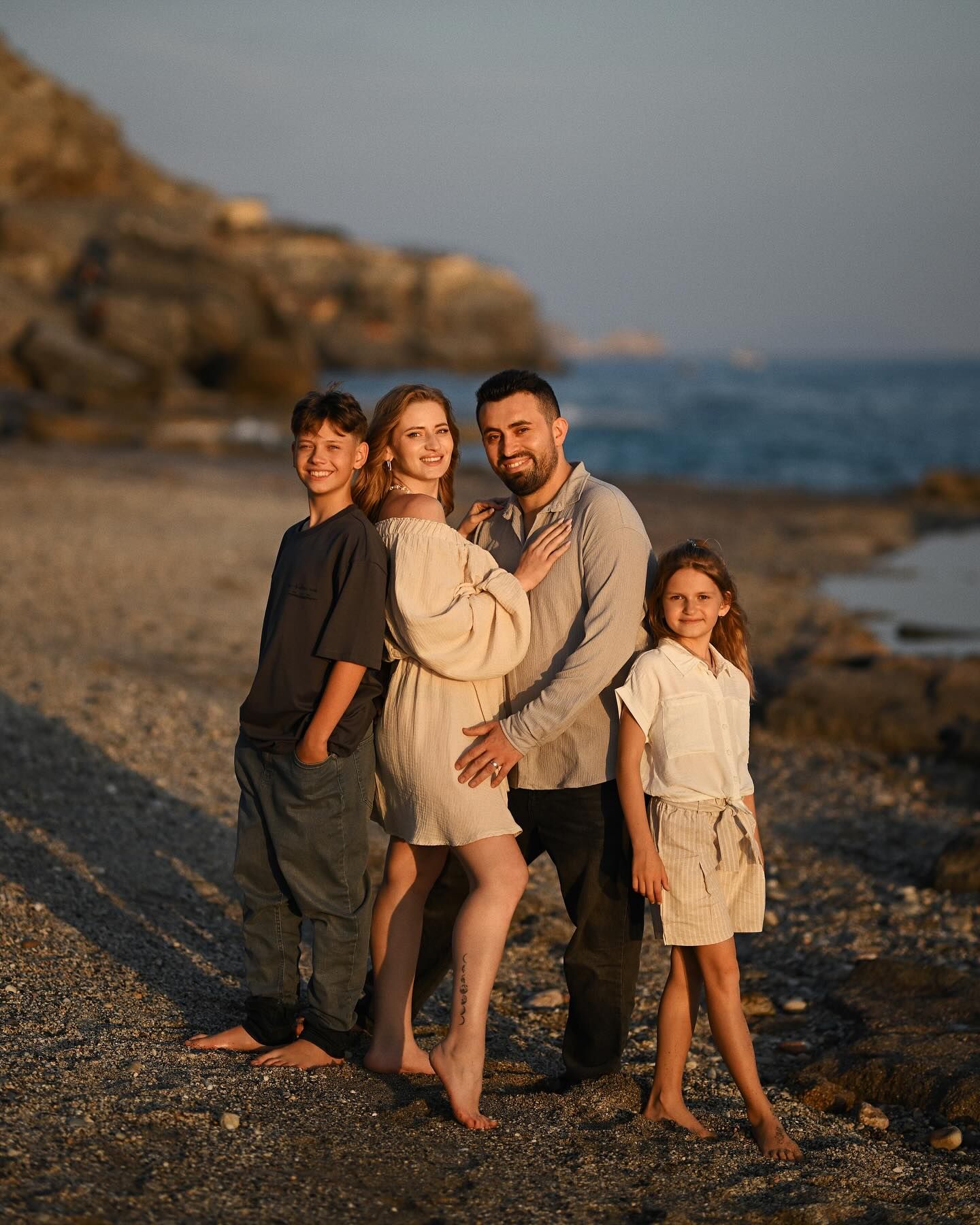 A happy family of four posing together on a rocky seashore during a golden hour photoshoot in Costa Blanca.