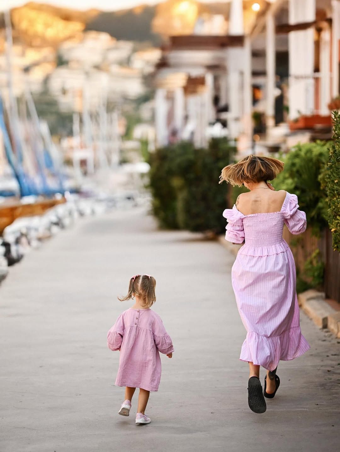 Back view of a mother and daughter running hand in hand along the wooden pier of the Port Saplaya harbor during their session