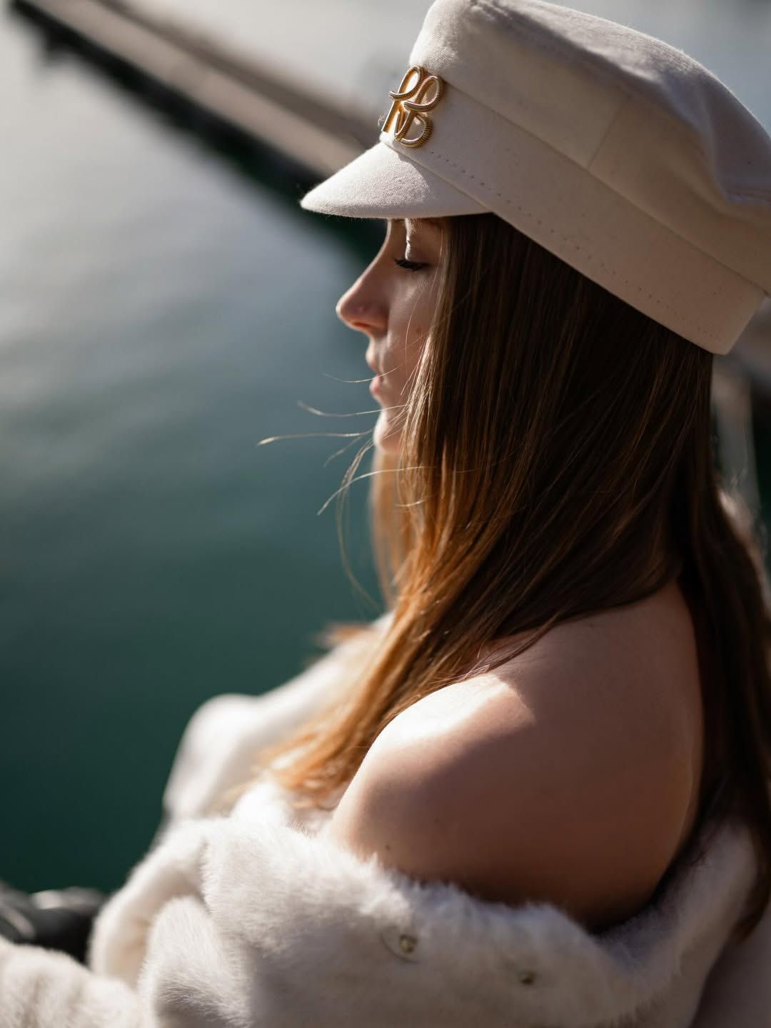 Close-up profile portrait of a woman in a white cap by the blue canal water at the Marina in Valencia