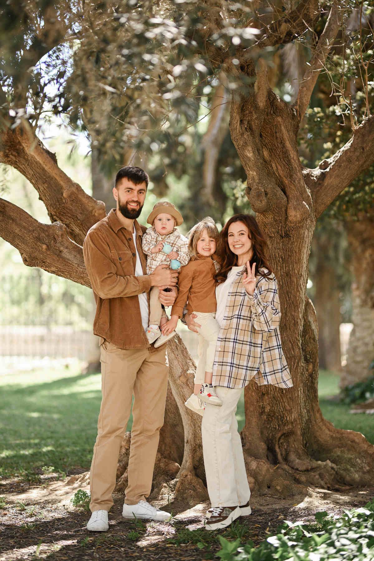 A happy family of four posing together for a portrait in front of a massive historic tree in Jardines del Real.