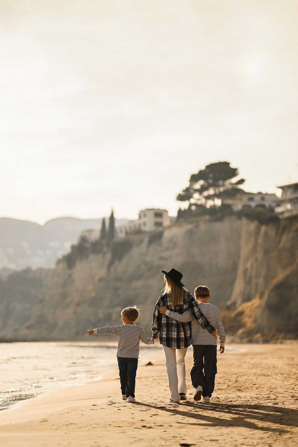 A mother and her two boys walking together along the shoreline, enjoying the peaceful coastal views of Calpe at golden hour