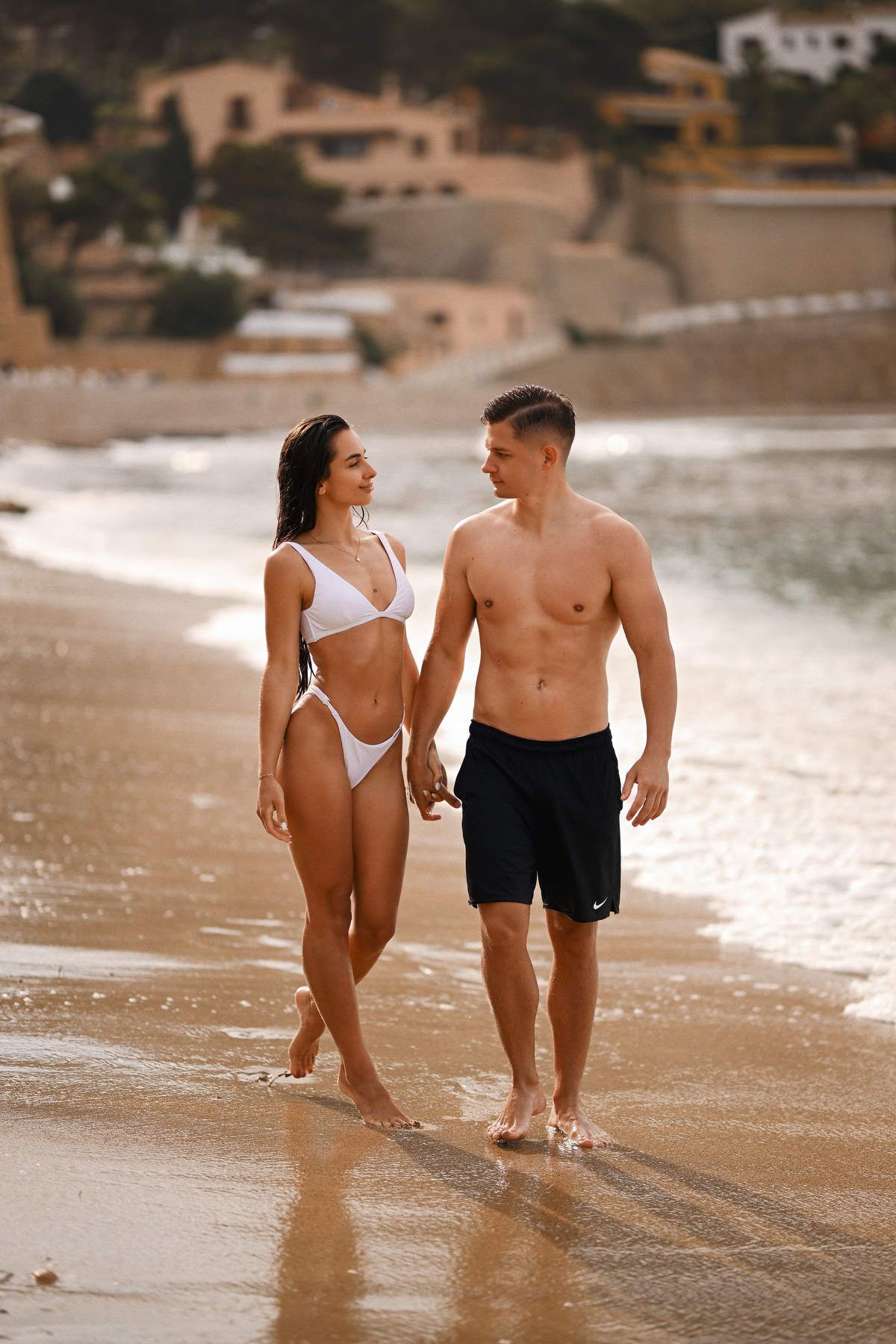 A romantic couple holding hands and walking out of the sea during a lifestyle photoshoot at Playa del Portet in Moraira