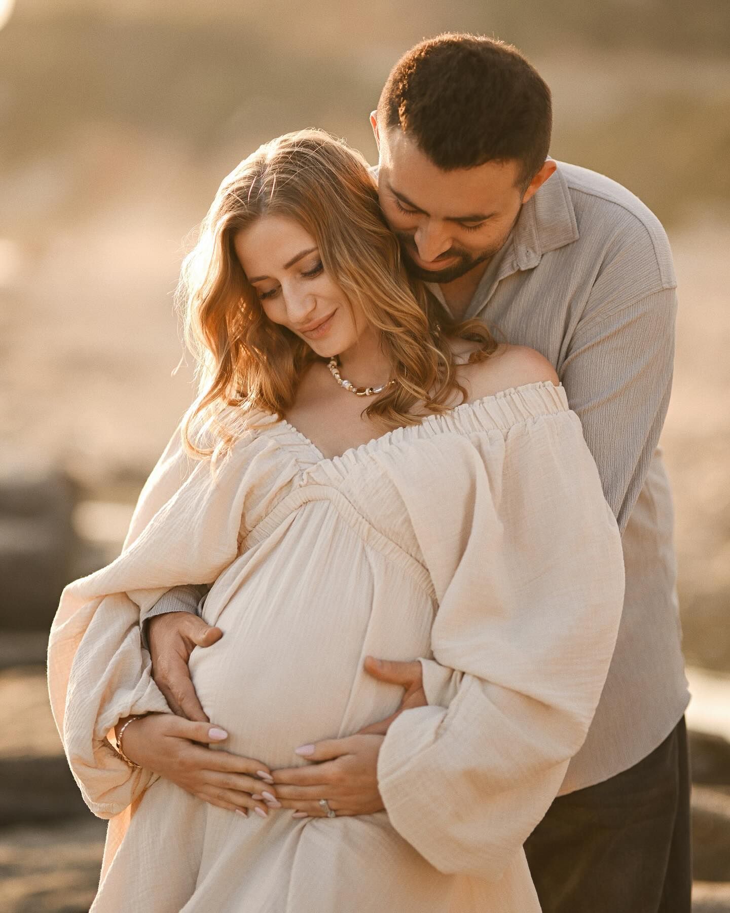 Close-up portrait of a husband embracing his pregnant wife's belly during a warm sunset photoshoot on the Costa Blanca coast.