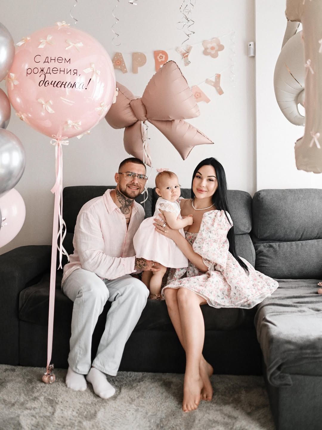 Beautiful family portrait of parents with their one-year-old child sitting on a couch decorated with party balloons.