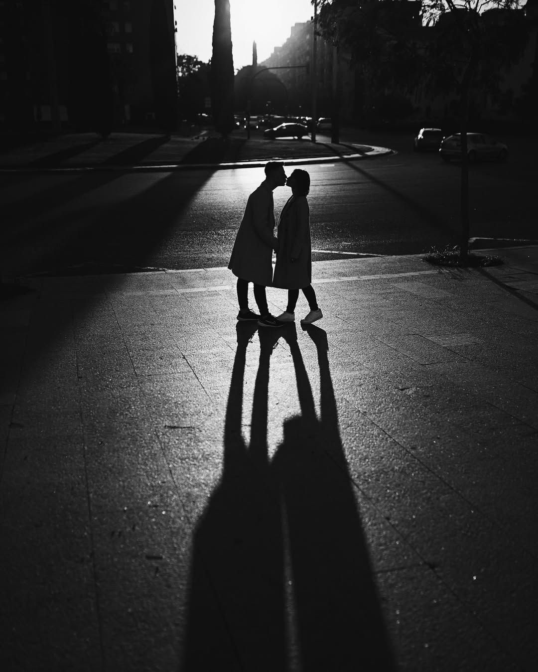 Black and white silhouette of a couple kissing on a sunlit city street corner during an urban engagement session in Valencia.