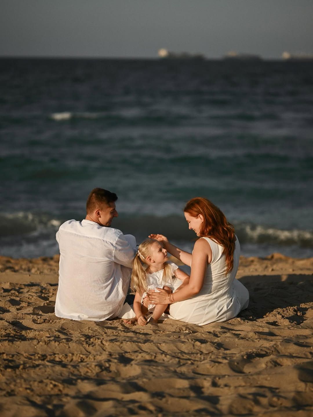 A family sitting together on the sandy beach of El Saler while watching the sunset over the Mediterranean sea.