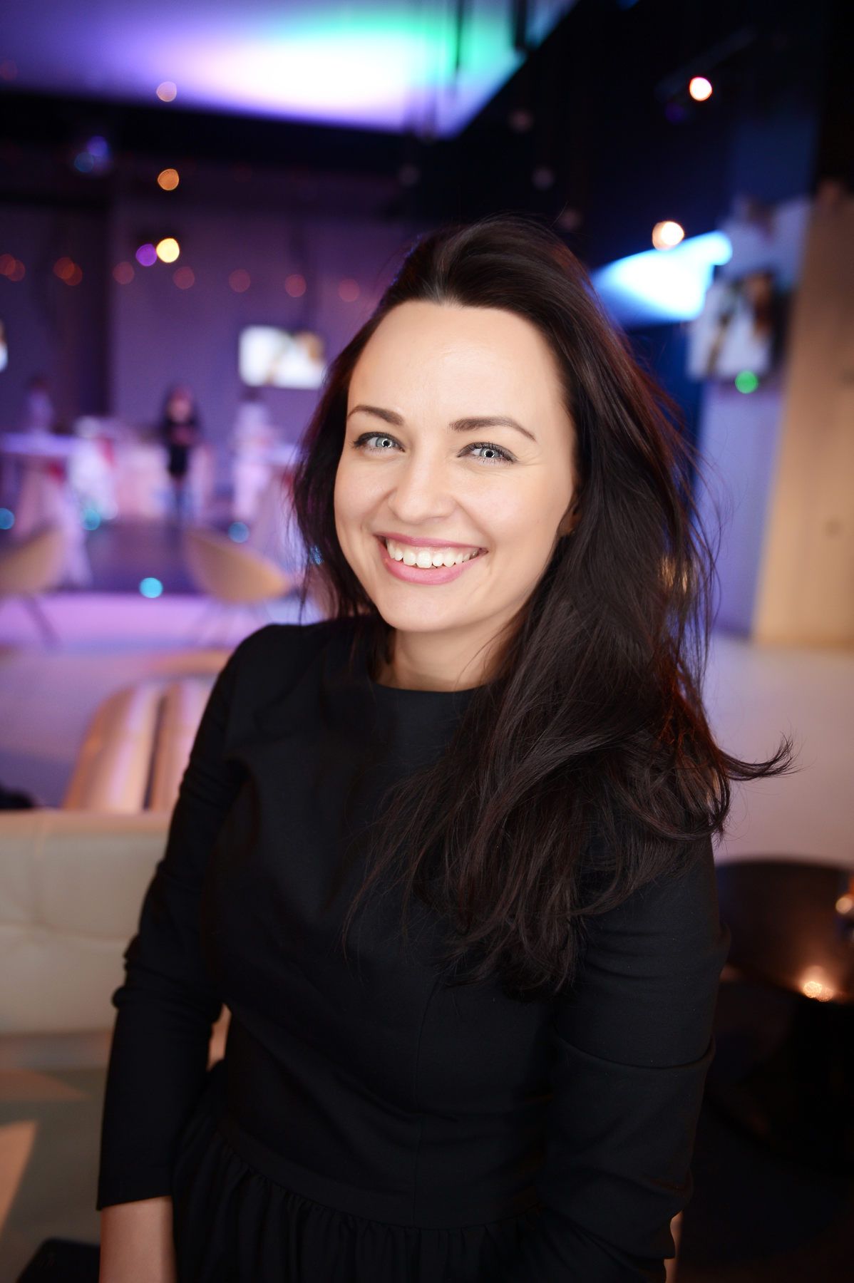 Close-up portrait of a smiling female guest in a black dress at a vibrant evening party in Valencia.