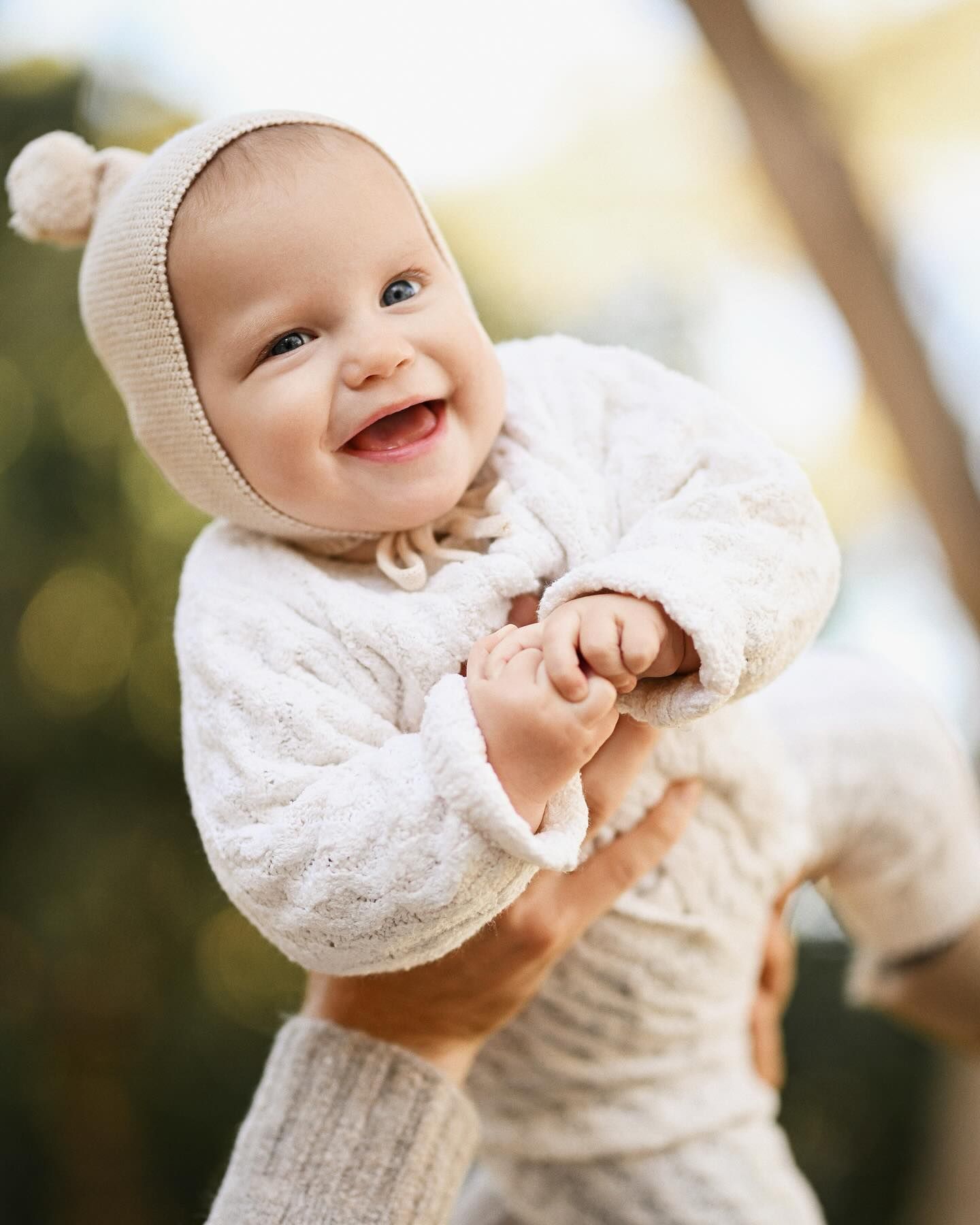 Close-up of a laughing baby wearing a knit bonnet with pom-poms during a 2 to 6 months baby session in Valencia.