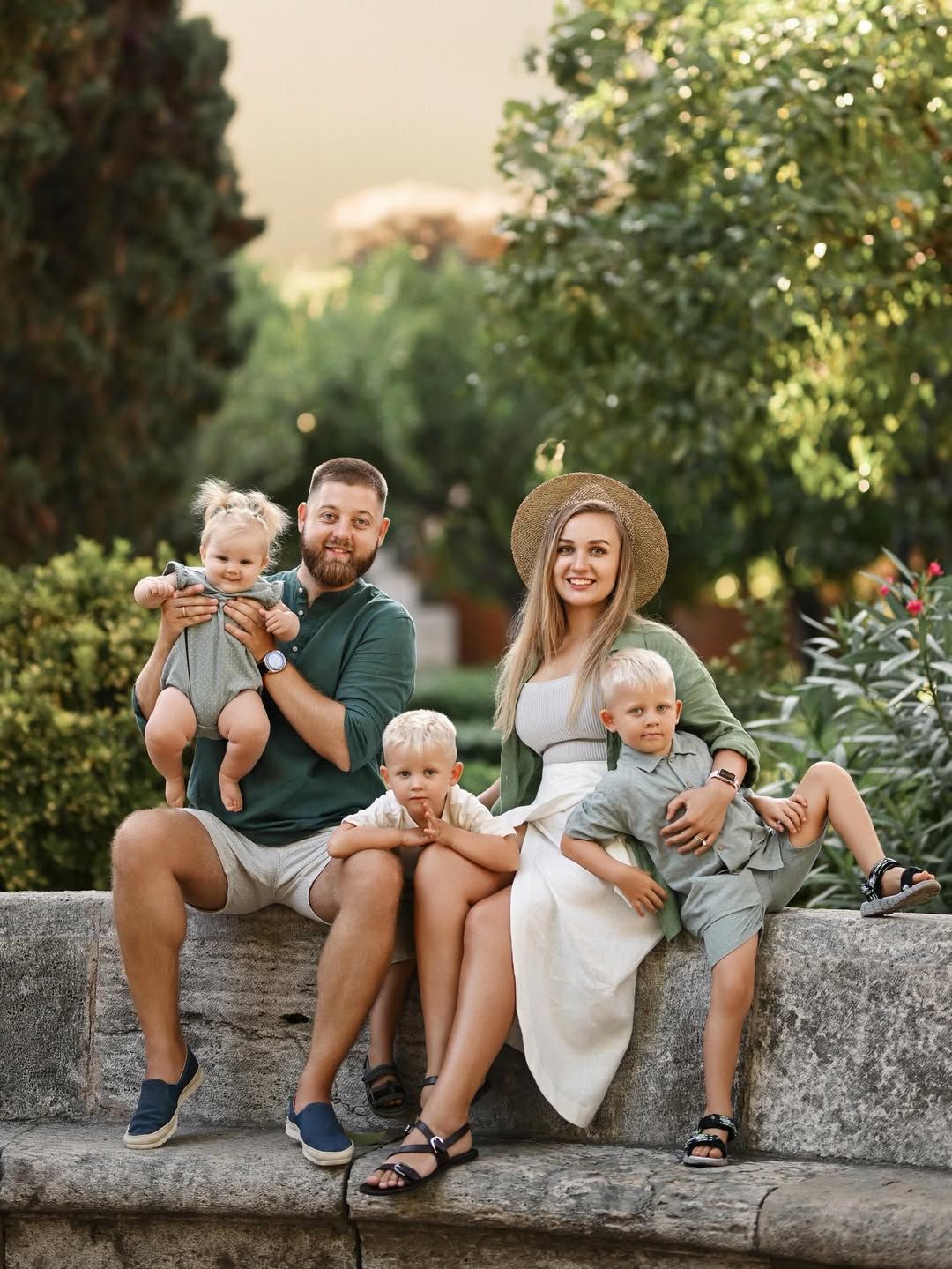 A family of five sitting on a stone wall in Turia Park, Valencia during a relaxed outdoor family photo session.