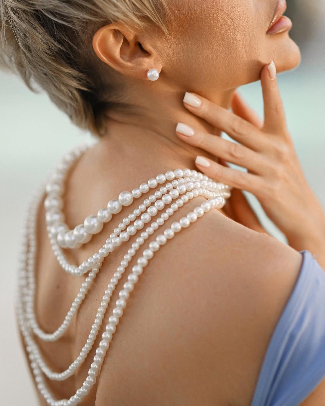 Close-up beauty portrait of a blonde woman looking into the camera, showcasing layered pearls and an open shoulder