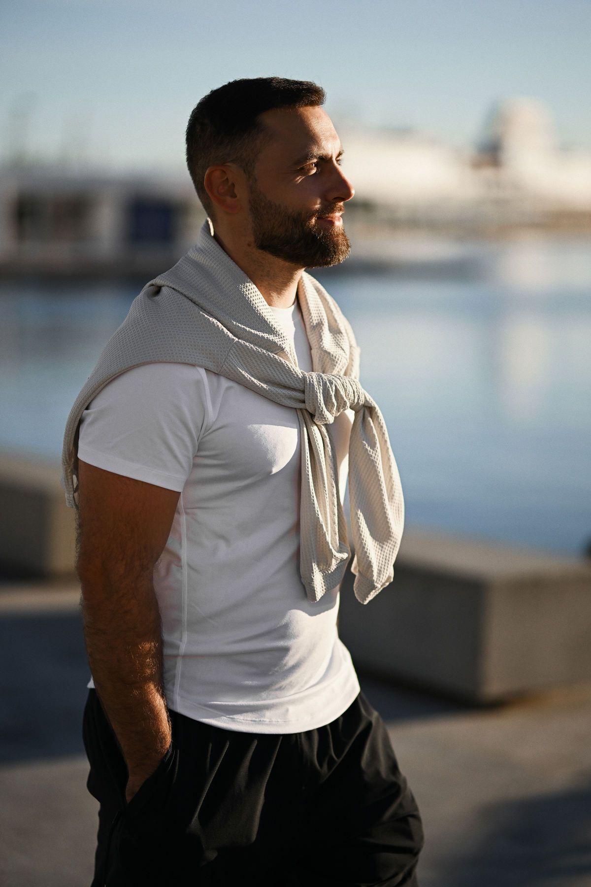 Casual men's style portrait with backlighting in Valencia, featuring a man with a sweater tied over his shoulders looking sharp.