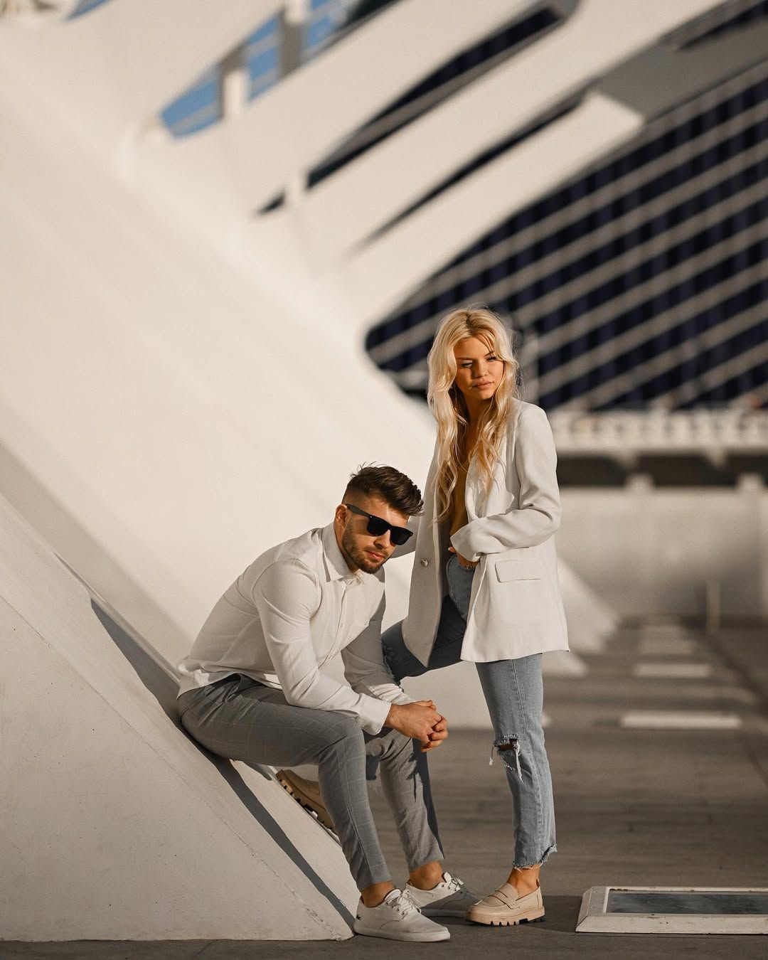 Editorial couples session featuring a man sitting on an angled white architectural curve while a woman stands beside him