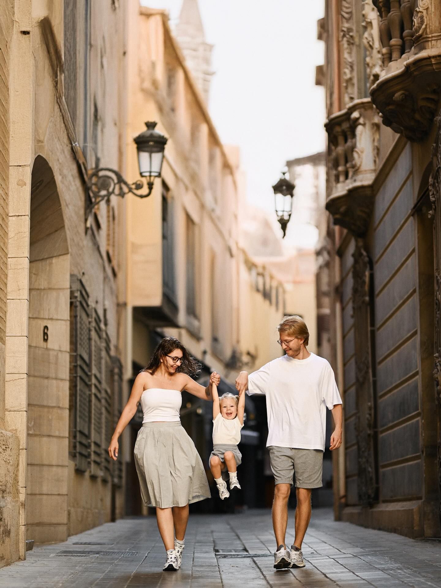 arents happily holding their laughing toddler’s hands while walking a beautiful historic narrow street during a Valencia city photoshoot.