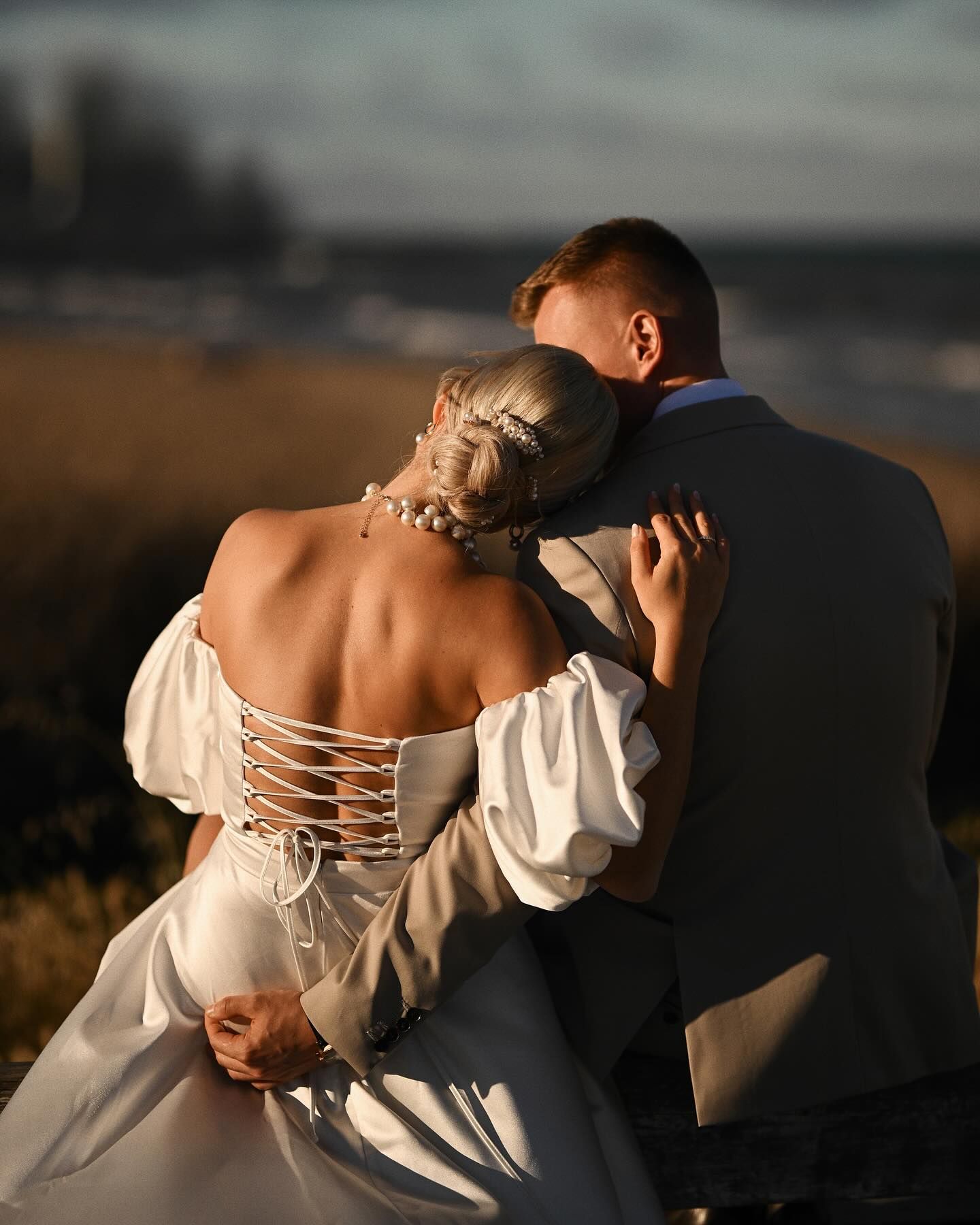 A cinematic wedding portrait of an eloping couple sitting on a bench with their backs turned, looking at the calm sea in Valencia.