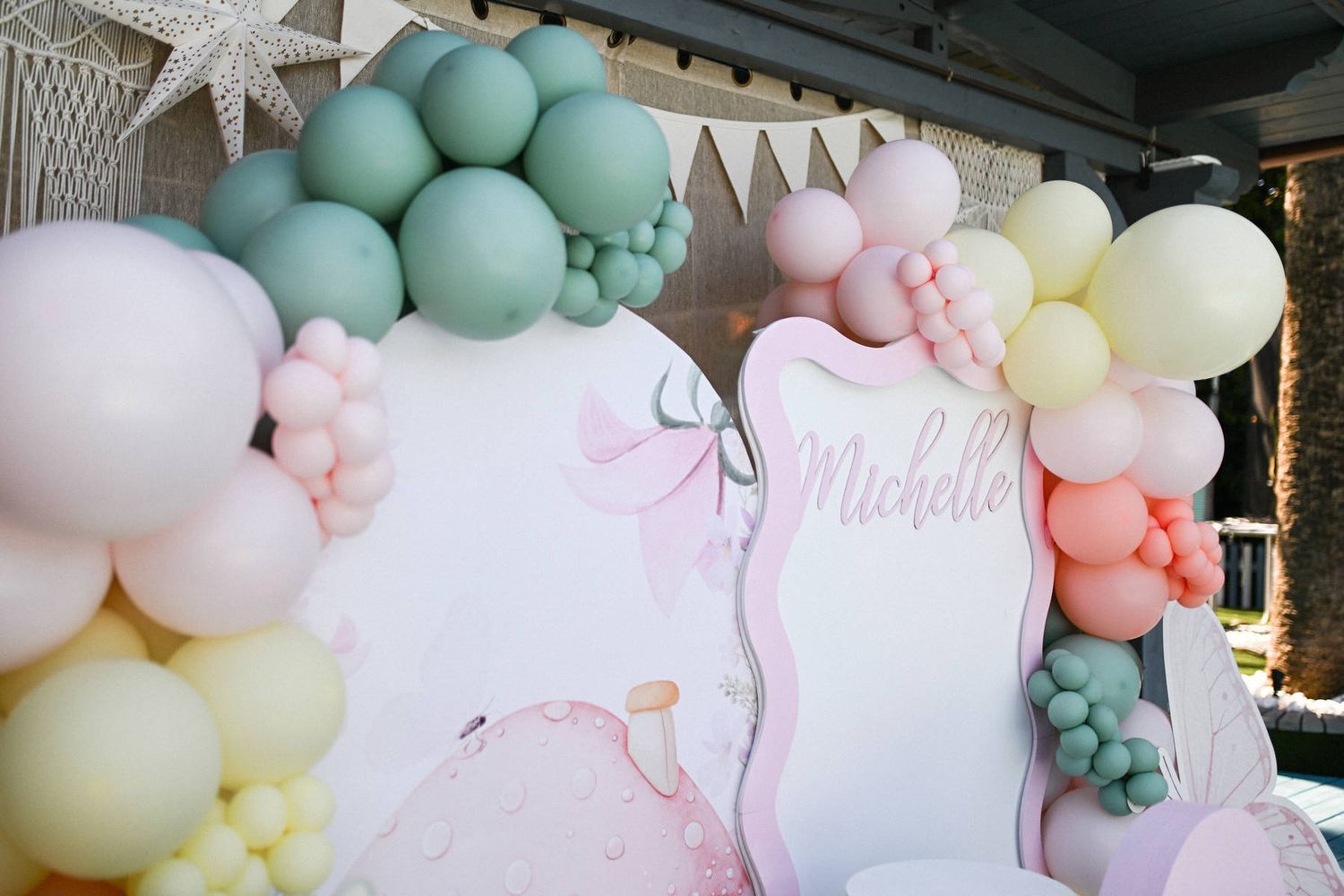 Close-up of a customized fairytale birthday backdrop decorated with pastel pink, yellow, and mint green balloon garlands.