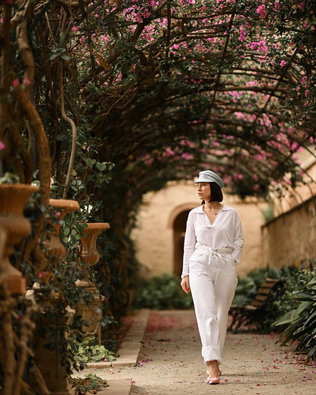 A girl walking under a romantic canopy of blooming pink flowers in Monforte Gardens.