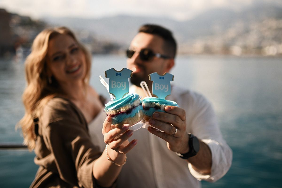 Close up of a smiling expecting couple holding blue 'Boy' cupcakes to announce their baby's gender in Valencia.