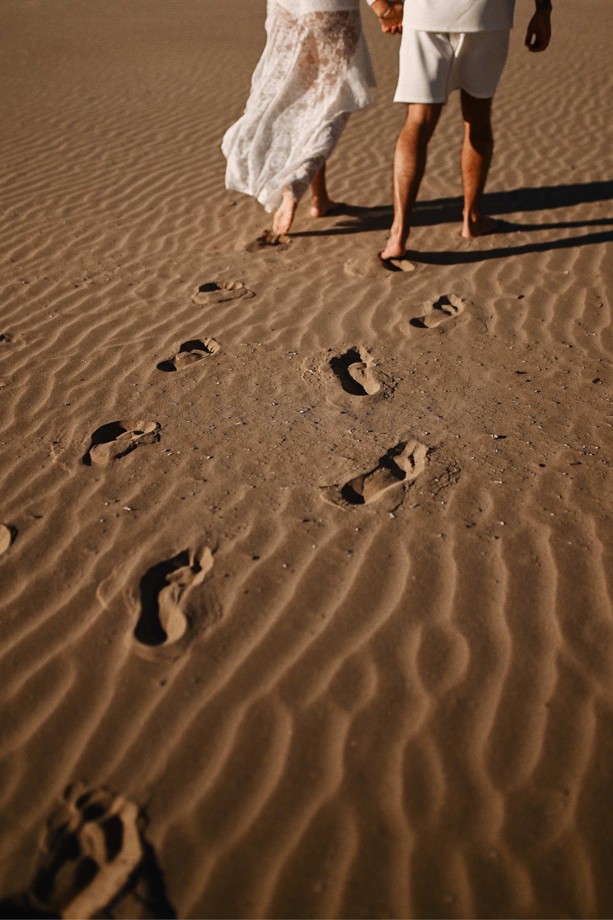 A romantic shot focusing on the footsteps of an expectant couple walking along the sandy beach during sunset.
