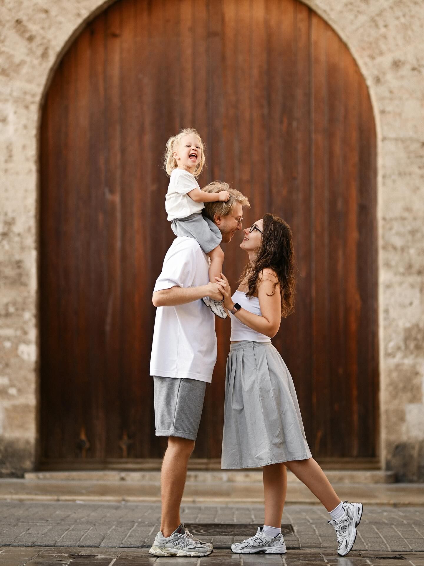 A joyful family portrait with a toddler sitting on her father’s shoulders in front of  antique wooden door in the Valencia city center.