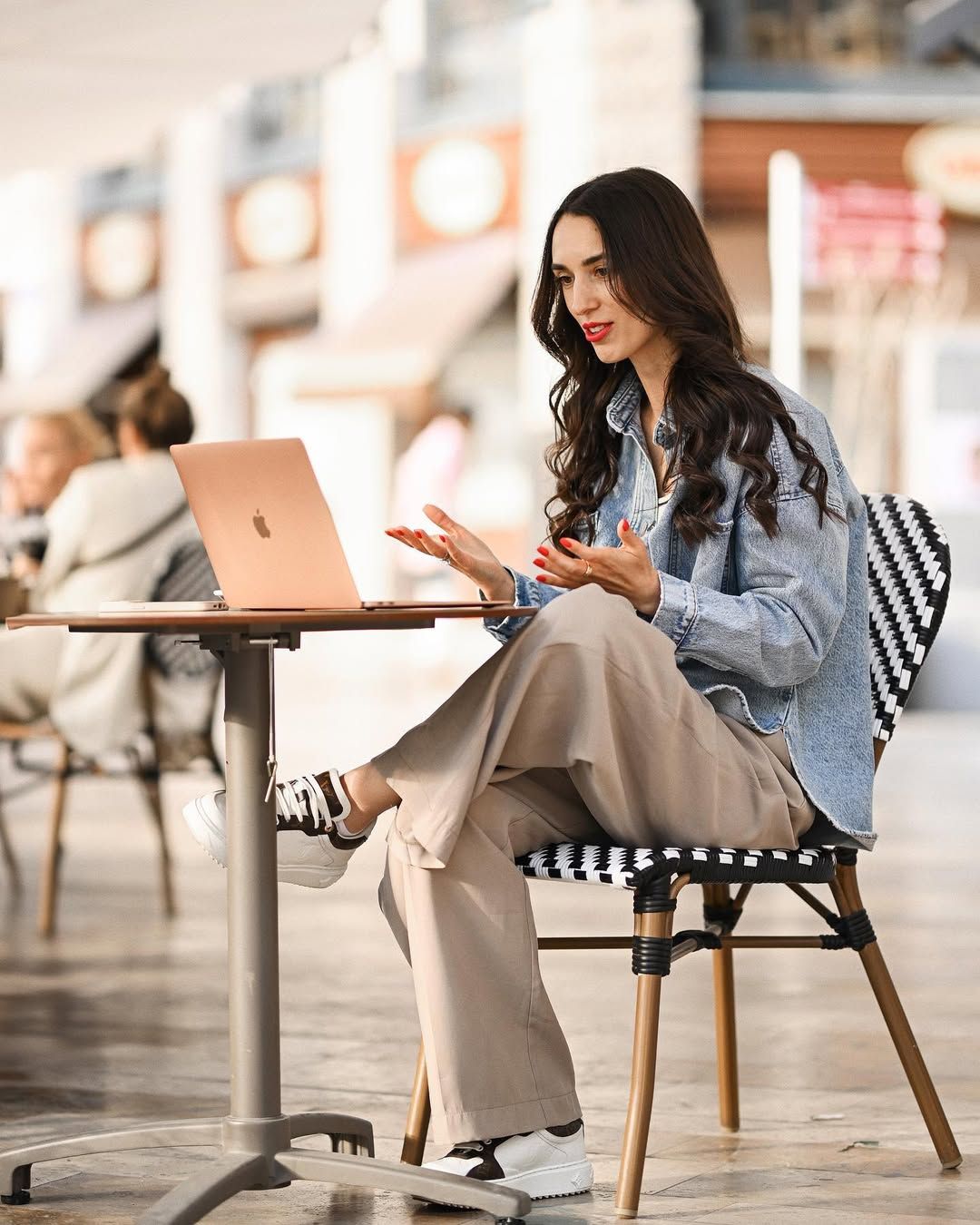 Female online educator gesturing during a laptop video call at an outdoor cafe in Valencia. Personal branding photoshoot