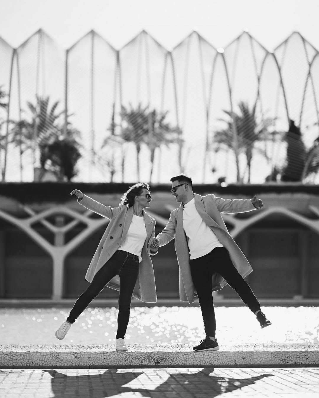Playful black and white shot of a couple balancing on a low wall near the reflective pools at the City of Arts and Sciences