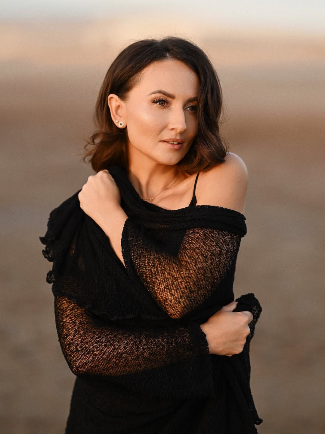 Women's portrait session at a Valencia beach during golden hour, woman looking away wrapped in a dark textured shawl.