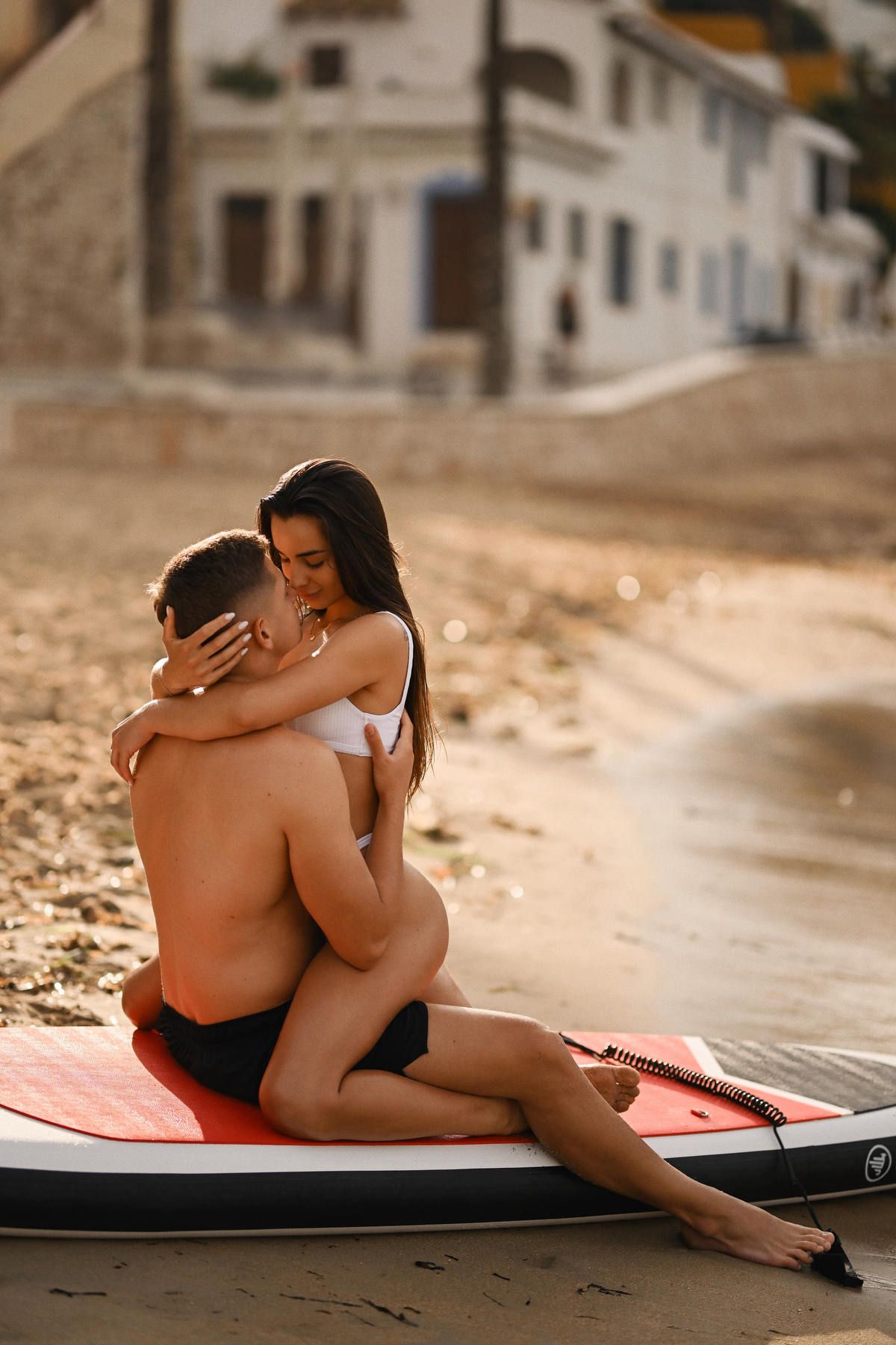 Romantic couple embracing on a paddleboard on the sand at Playa del Portet during a golden hour session