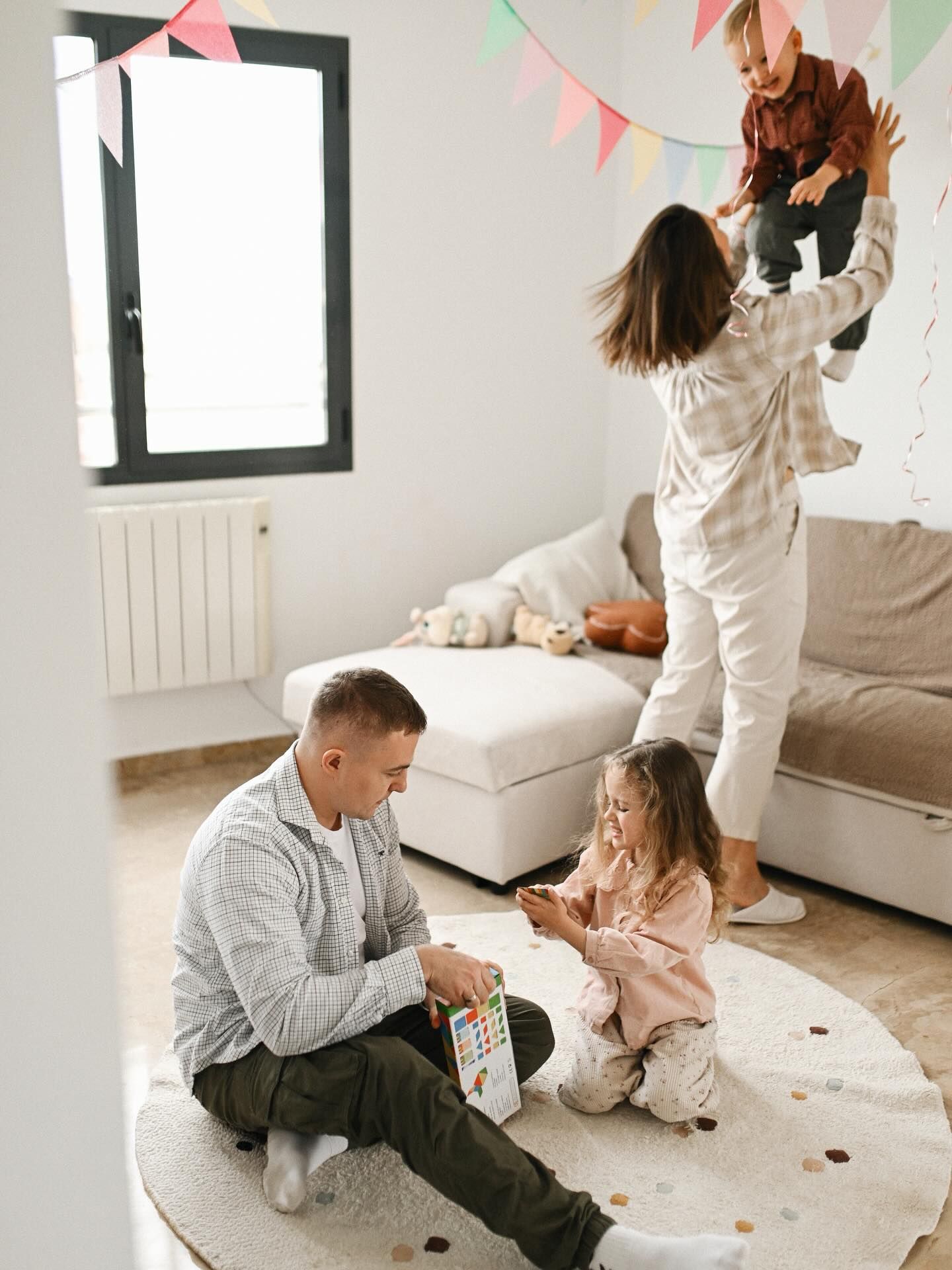 A father playing with his daughter on the floor while a mother lifts their son up in the air during a fun family home photography session.