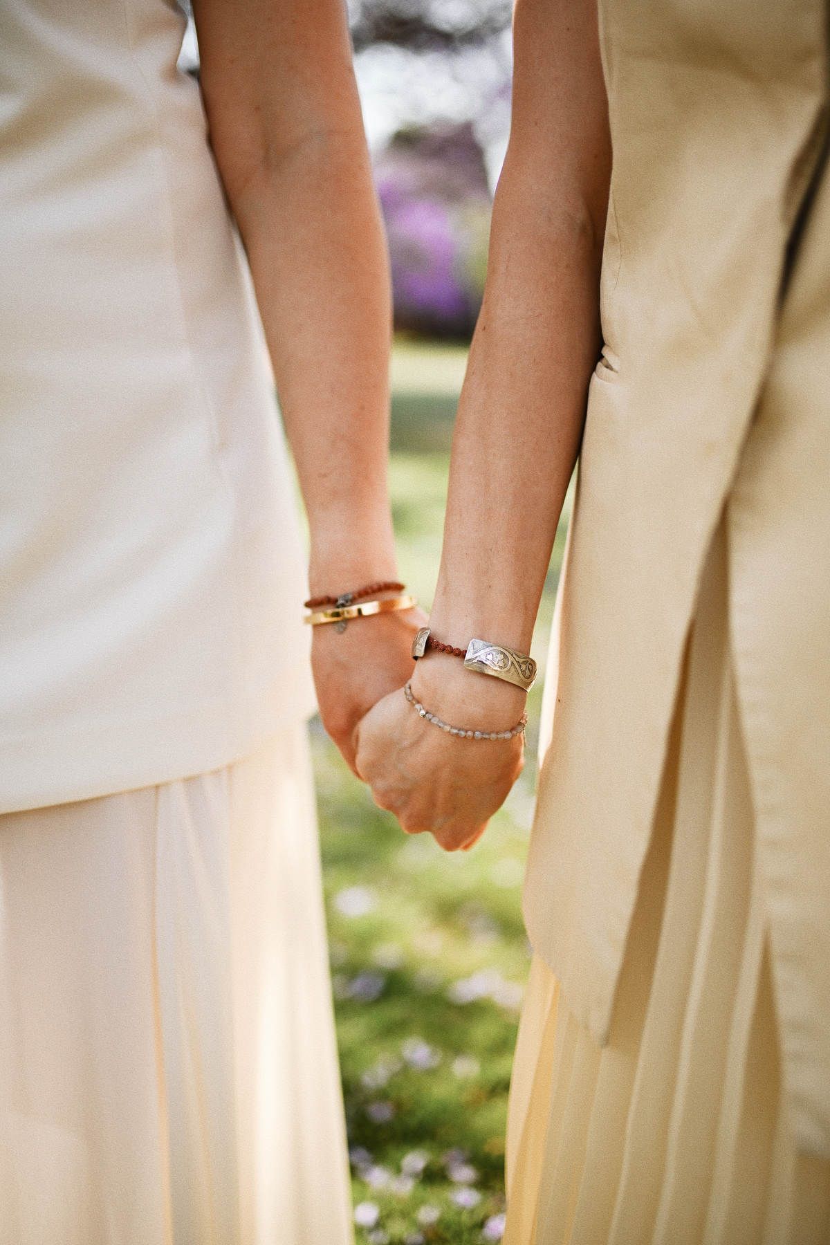 Close-up macro photograph of two adult sisters holding hands, showcasing their delicate silver and gold bracelets.